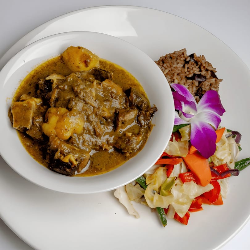 Curried goat with potatoes, rice and peas, and steamed vegetables, garnished with an orchid.