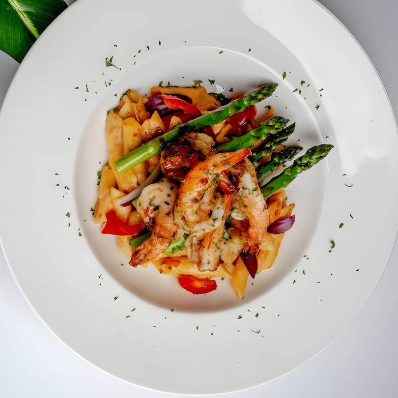 Grilled shrimp and asparagus served over pasta with red peppers and onions on a white plate.