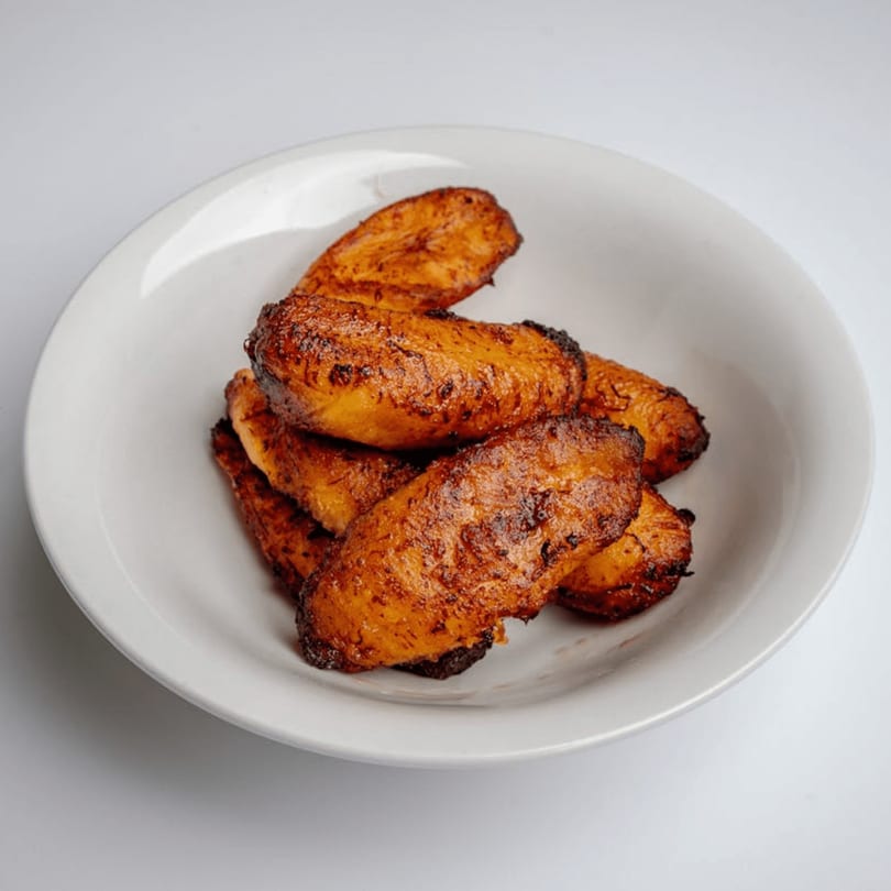 A white bowl filled with several pieces of golden-brown, caramelized fried plantains.