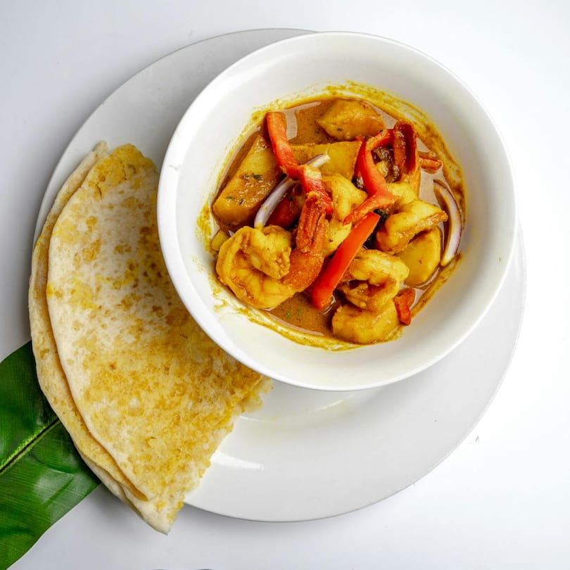 Caribbean shrimp curry with potatoes, red peppers, and onions, served with flatbread on a white plate.