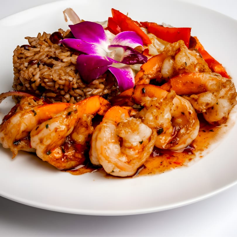 Caribbean jerk shrimp with rice and peas, garnished with a purple orchid and red bell peppers.