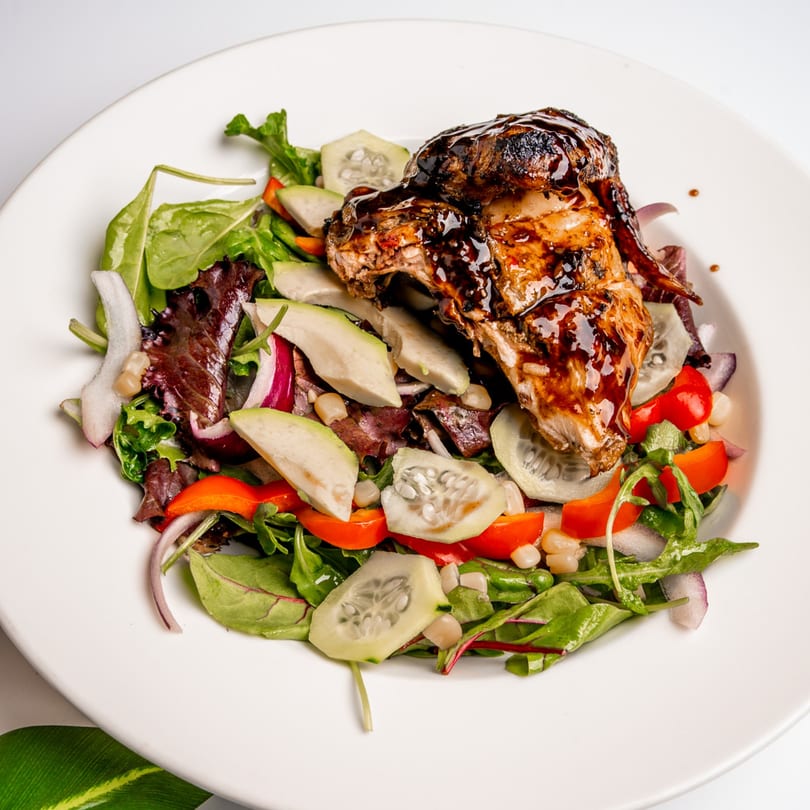 Caribbean jerk chicken with a dark glaze, served on a fresh salad with avocado, cucumber, and red peppers.